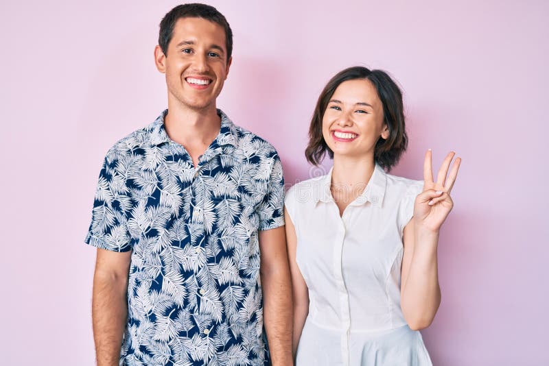 Bella coppia che indossa vestiti casuali che si presenta e punta con le dita numero tre mentre sorride sicura e felice fotografia stock libera da diritti