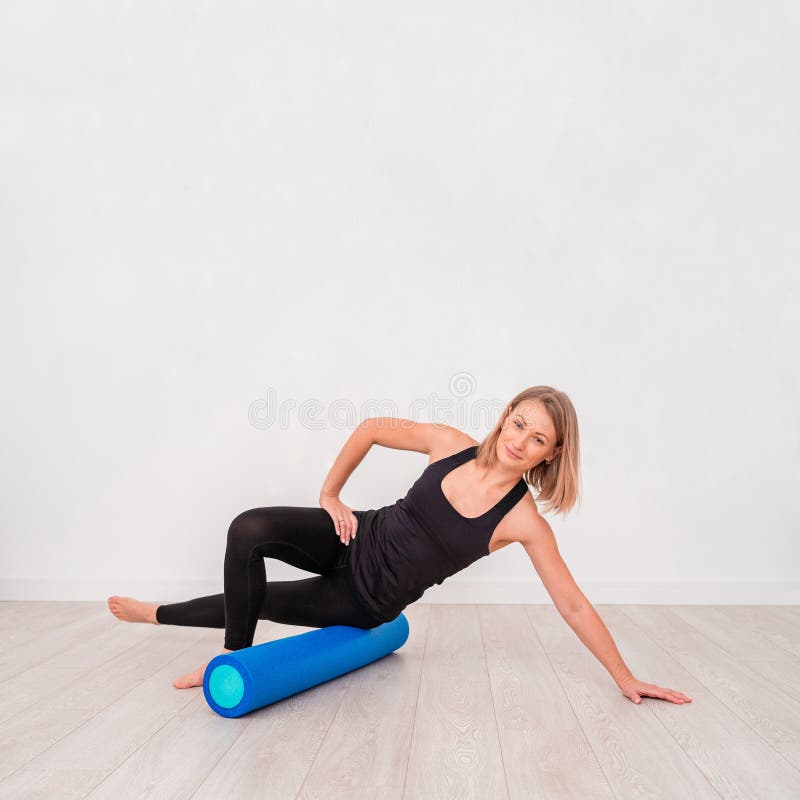 Bella donna in abiti sportivi, istruttore di Pilates che allunga e che si scalda con il rullo della schiuma