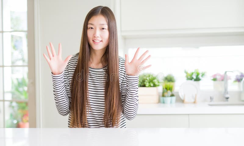 Bella donna asiatica che indossa un maglione a strisce che mostra e punta con le dita numero dieci, sorridendo sicura e felice fotografia stock
