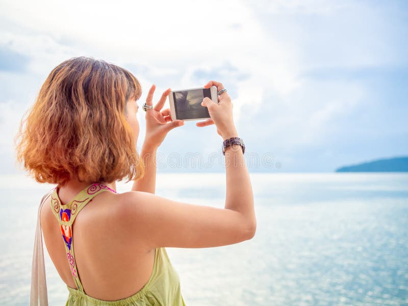 Bella donna asiatica con i capelli di scarsità facendo uso dello Smart Phone considerare di vista sul mare della foto fotografia stock Bella donna asiatica con i capelli di scarsità facendo uso dello Smart Phone considerare di vista sul mare della foto fotografia stock