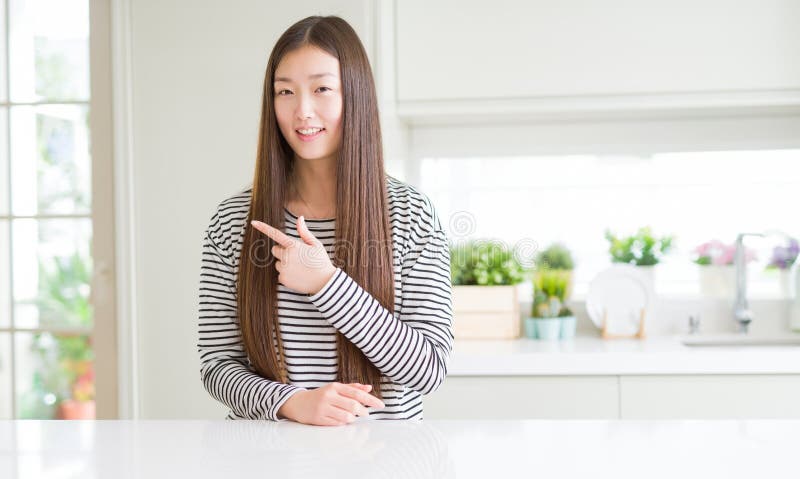 Bella donna asiatica con il maglione a strisce allegro con un sorriso di volto puntato con la mano e il dito verso l'alto con immagine stock