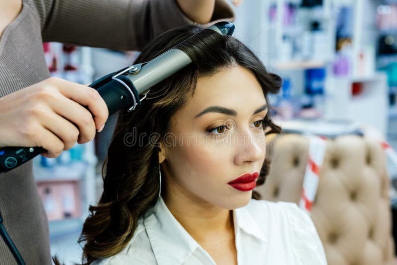 Bella donna brunetta in un salone di bellezza. Bella donna brunetta si ricuce i capelli con una ghisa ruscciante in un salone di bellezza..