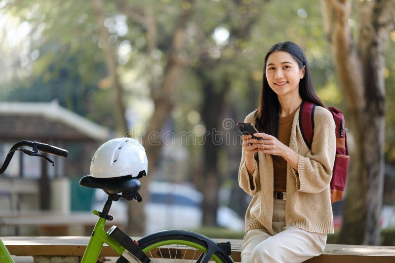 Bella donna che fa una passeggiata in bicicletta nel parco con una donna che tiene in mano uno smartphone con una donna affittuari immagine stock libera da diritti