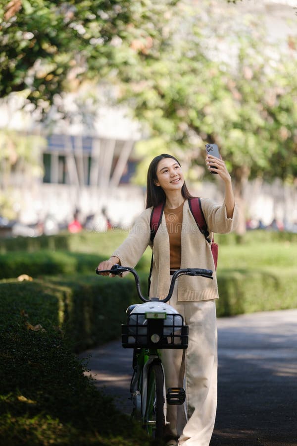 Bella donna che fa una passeggiata in bicicletta nel parco con una donna che tiene in mano uno smartphone con una donna affittuari fotografia stock