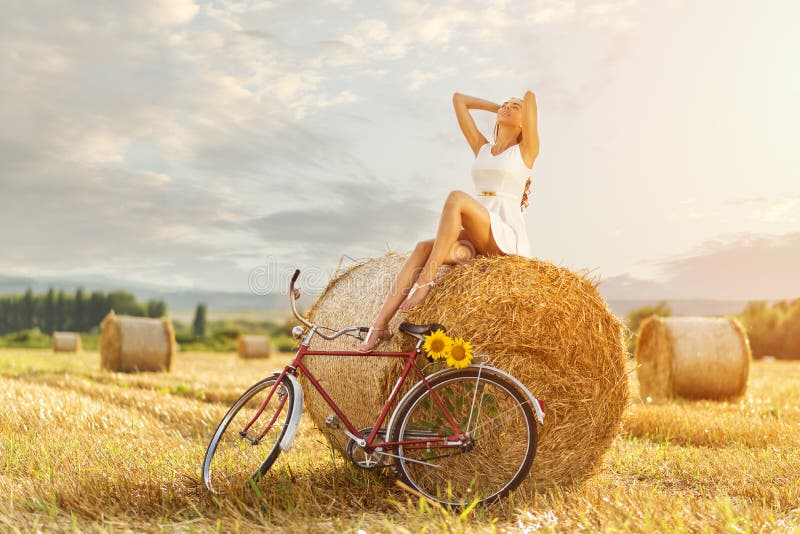 Bella donna che gode del sole in una balla della paglia, accanto alla vecchia bicicletta rossa