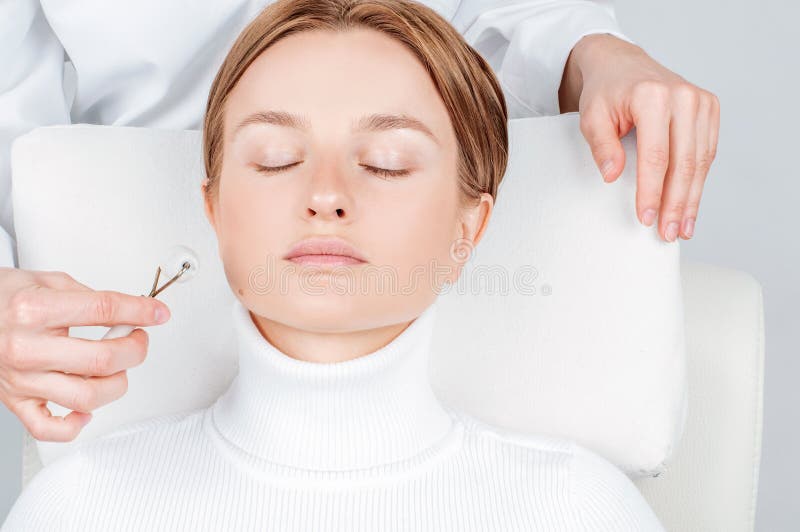 Bella donna che ha trattamento del fronte, cosmetologo che massaggia fronte con i rulli della giada immagine stock libera da diritti Bella donna che ha trattamento del fronte, cosmetologo che massaggia fronte con i rulli della giada immagine stock libera da diritti
