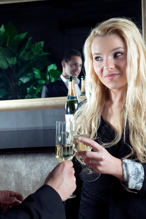 Beautiful young blond women toasting her partner, a handsome men who is reflected in the mirror, with flutes of golden champagne as they celebrate a special moment. Beautiful young blond women toasting her partner, a handsome men who is reflected in the mirror, with flutes of golden champagne as they celebrate a special moment