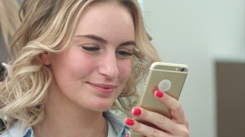 Bella donna che usa lo smartphone in un salone di bellezza, mentre ha un parrucchiere