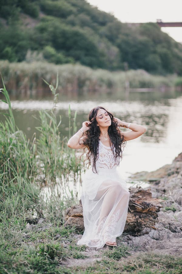 Bella donna con capelli ricci lunghi vestiti in vestito da stile di boho che posa vicino al lago immagini stock Bella donna con capelli ricci lunghi vestiti in vestito da stile di boho che posa vicino al lago immagini stock