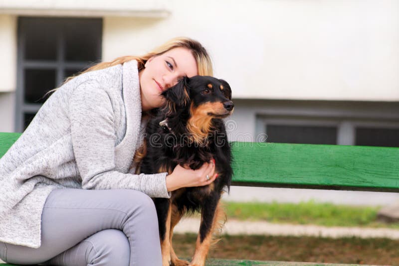 Bella donna con il suo piccolo cane misto della razza che si siede e che posa davanti alla macchina fotografica sul banco di legn fotografie stock libere da diritti Bella donna con il suo piccolo cane misto della razza che si siede e che posa davanti alla macchina fotografica sul banco di legn fotografie stock libere da diritti