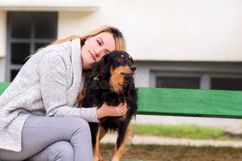 Bella donna con il suo piccolo cane misto della razza che si siede e che posa davanti alla macchina fotografica sul banco di legn immagini stock libere da diritti Bella donna con il suo piccolo cane misto della razza che si siede e che posa davanti alla macchina fotografica sul banco di legn immagini stock libere da diritti