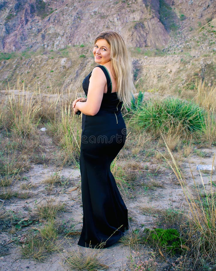Bella donna grassottella in un vestito nero Bionda Con un bello sorriso All'aperto su una prateria immagini stock libere da diritti Bella donna grassottella in un vestito nero Bionda Con un bello sorriso All'aperto su una prateria immagini stock libere da diritti