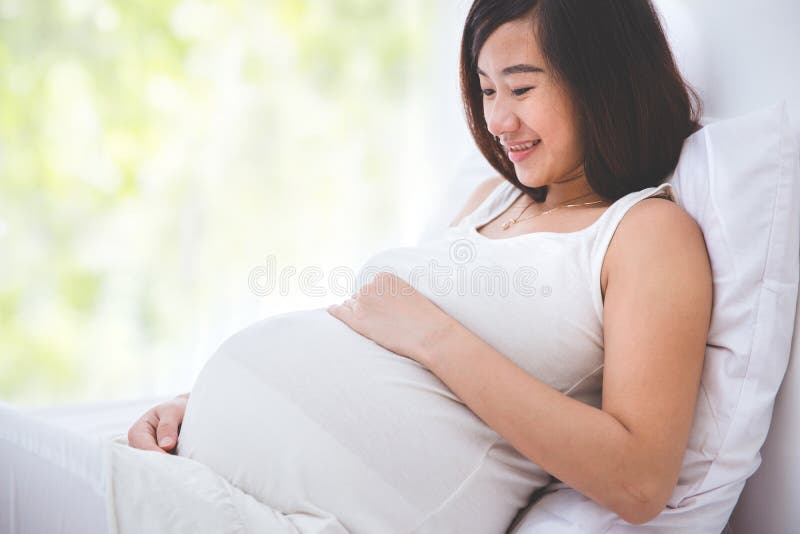 Bella donna incinta che sorride esaminando la sua pancia fotografia stock libera da diritti Bella donna incinta che sorride esaminando la sua pancia fotografia stock libera da diritti