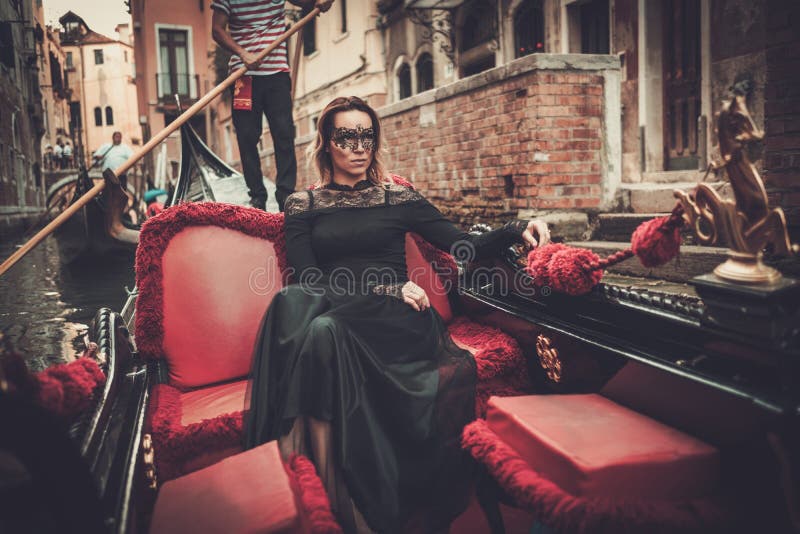 Bella donna in vestito nero con la guida carnaval della maschera sulla gondola fotografia stock libera da diritti Bella donna in vestito nero con la guida carnaval della maschera sulla gondola fotografia stock libera da diritti