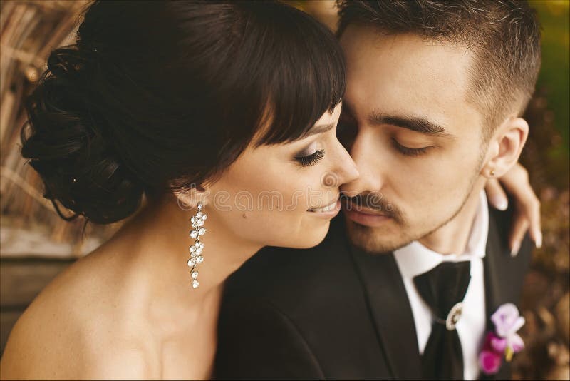 Bella e felice coppia appena sposata abbracciandosi e baciandosi, un bel ragazzo con un elegante vestito nero e giovane fotografia stock Bella e felice coppia appena sposata abbracciandosi e baciandosi, un bel ragazzo con un elegante vestito nero e giovane fotografia stock
