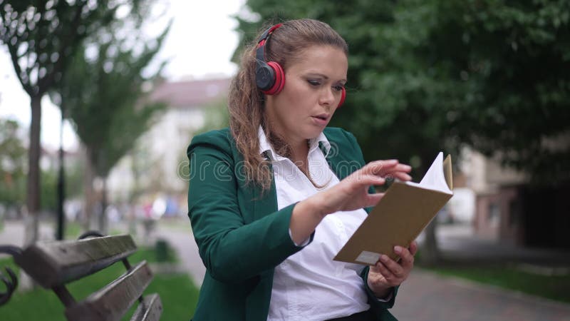 Bella e intelligente donna caucasica in cuffia che legge un libro in città all'aperto. assorbito