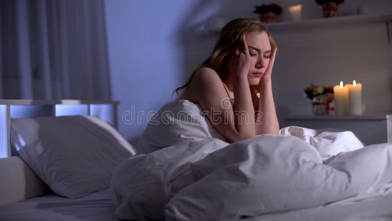 Bella emicrania di sofferenza della donna, sedentesi a letto, postumi di una sbornia o giorno stressante immagine stock Bella emicrania di sofferenza della donna, sedentesi a letto, postumi di una sbornia o giorno stressante immagine stock