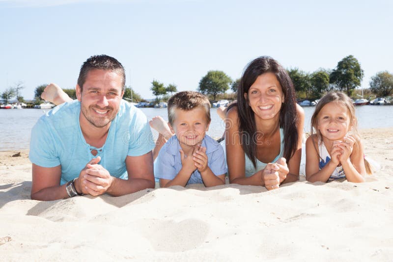 Bella famiglia felice con i bambini che si trovano insieme sulla spiaggia atlantica europea durante le vacanze estive fotografia stock Bella famiglia felice con i bambini che si trovano insieme sulla spiaggia atlantica europea durante le vacanze estive fotografia stock