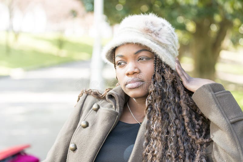 Bella giovane donna africana pensierosa con il cappello nel parco fotografia stock libera da diritti Bella giovane donna africana pensierosa con il cappello nel parco fotografia stock libera da diritti