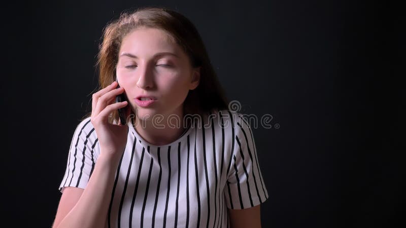 Bella giovane donna allegra dello zenzero che parla sul telefono, sorridere, stante sul fondo nero dello studio