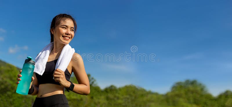 Bella giovane donna asiatica felice con il suo asciugamano bianco sopra il suo collo, condizione sorridente e tenente la sua bott immagine stock Bella giovane donna asiatica felice con il suo asciugamano bianco sopra il suo collo, condizione sorridente e tenente la sua bott immagine stock
