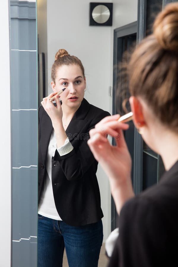 Bella giovane donna astuta diritta con un vestito che applica correttore fotografia stock libera da diritti Bella giovane donna astuta diritta con un vestito che applica correttore fotografia stock libera da diritti