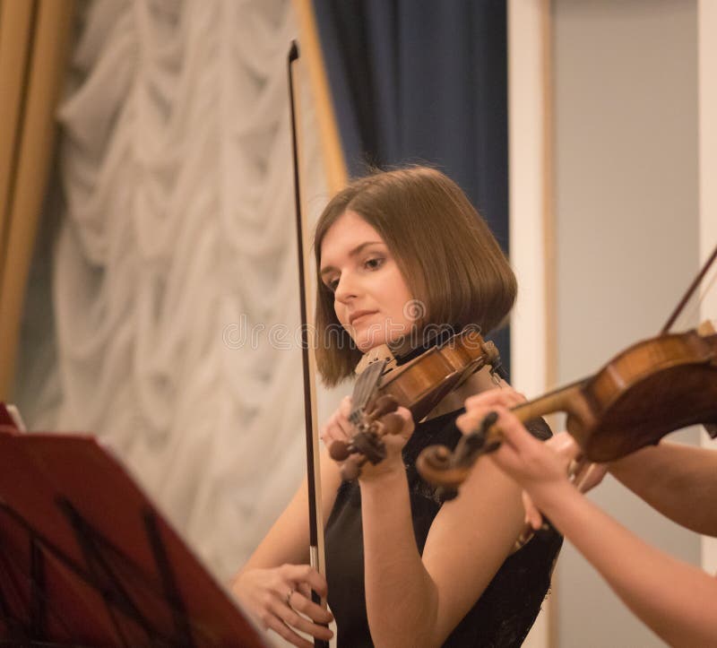 Bella giovane donna che gioca violino nella sala da concerto fotografie stock libere da diritti Bella giovane donna che gioca violino nella sala da concerto fotografie stock libere da diritti