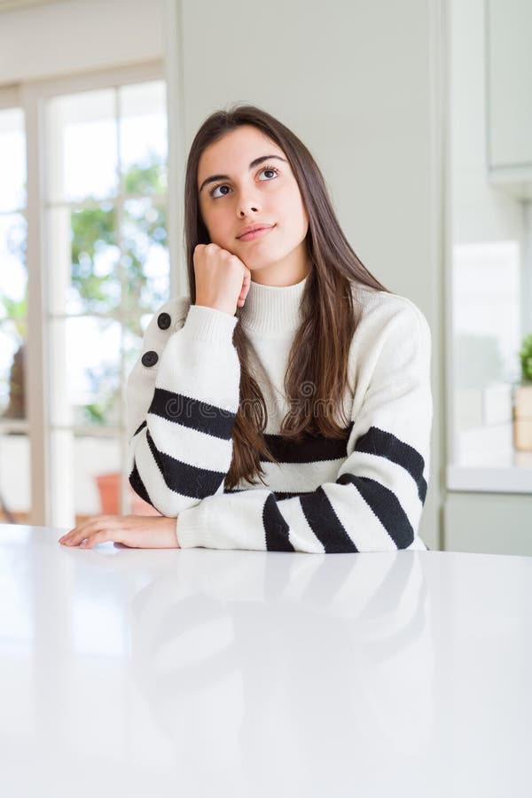 Bella giovane donna che indossa un pullover a strisce con mano sul mento pensando alla domanda espressione pensante immagini stock libere da diritti