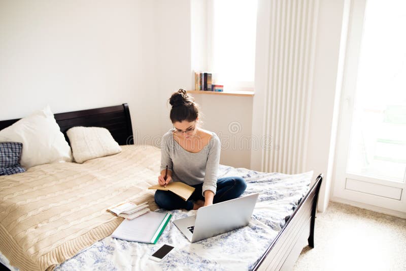 Bella giovane donna che si siede sul letto, lavorante Ministero degli Interni fotografia stock libera da diritti Bella giovane donna che si siede sul letto, lavorante Ministero degli Interni fotografia stock libera da diritti