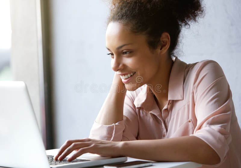 Bella giovane donna che sorride e che esamina lo schermo del computer portatile