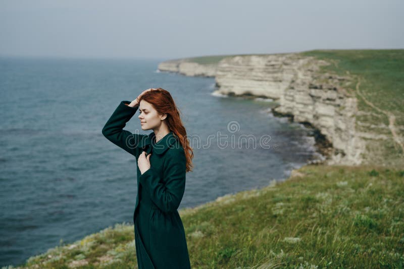 Bella giovane donna che sta su una scogliera vicino al mare immagini stock Bella giovane donna che sta su una scogliera vicino al mare immagini stock