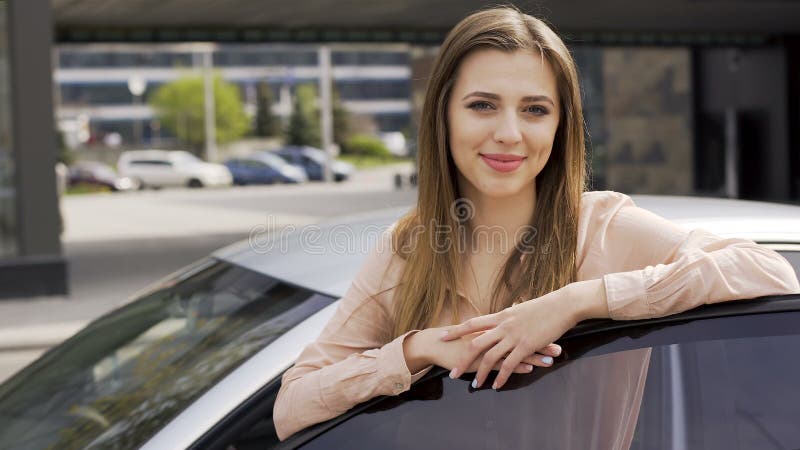 Bella giovane donna che sta vicino all'auto e che posa per la macchina fotografica Acquisto dell'automobile