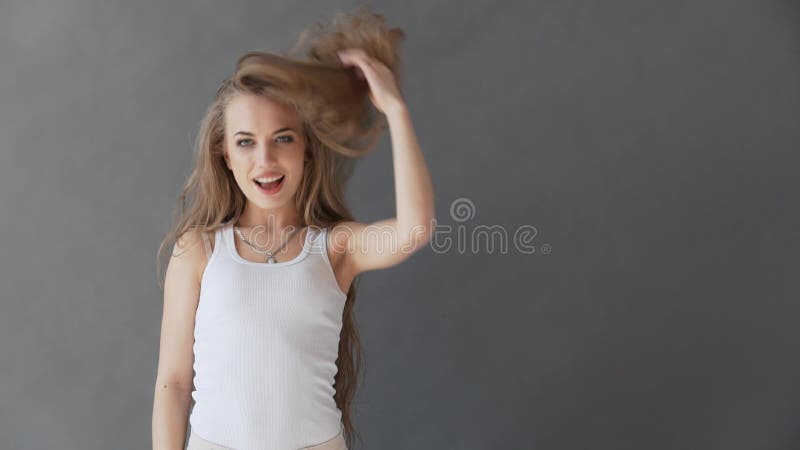 Bella giovane donna con capelli biondi sani In una canottiera sportiva bianca su un fondo grigio, posante sulla macchina fotograf