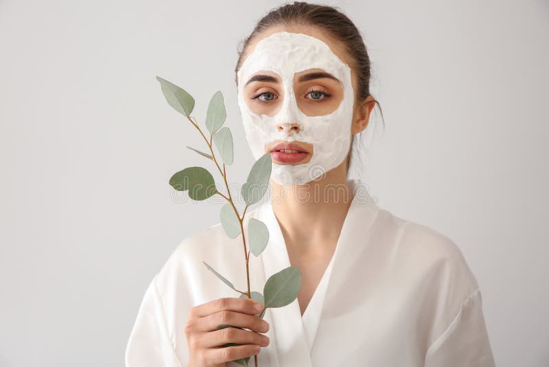 Bella giovane donna con il ramo facciale dell'eucalyptus e della maschera su fondo leggero immagine stock libera da diritti Bella giovane donna con il ramo facciale dell'eucalyptus e della maschera su fondo leggero immagine stock libera da diritti