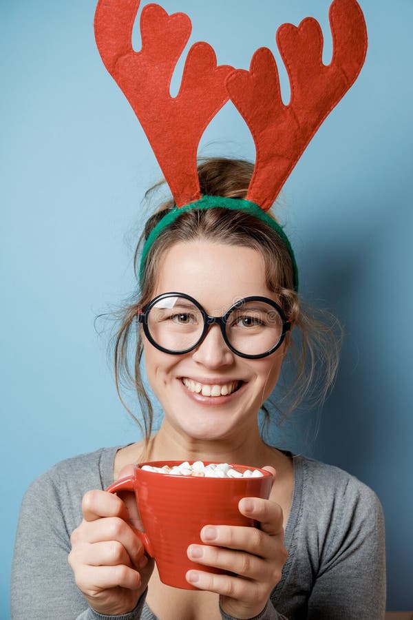 Bella giovane donna in corni di Natale con una tazza rossa su un blu fotografia stock libera da diritti Bella giovane donna in corni di Natale con una tazza rossa su un blu fotografia stock libera da diritti
