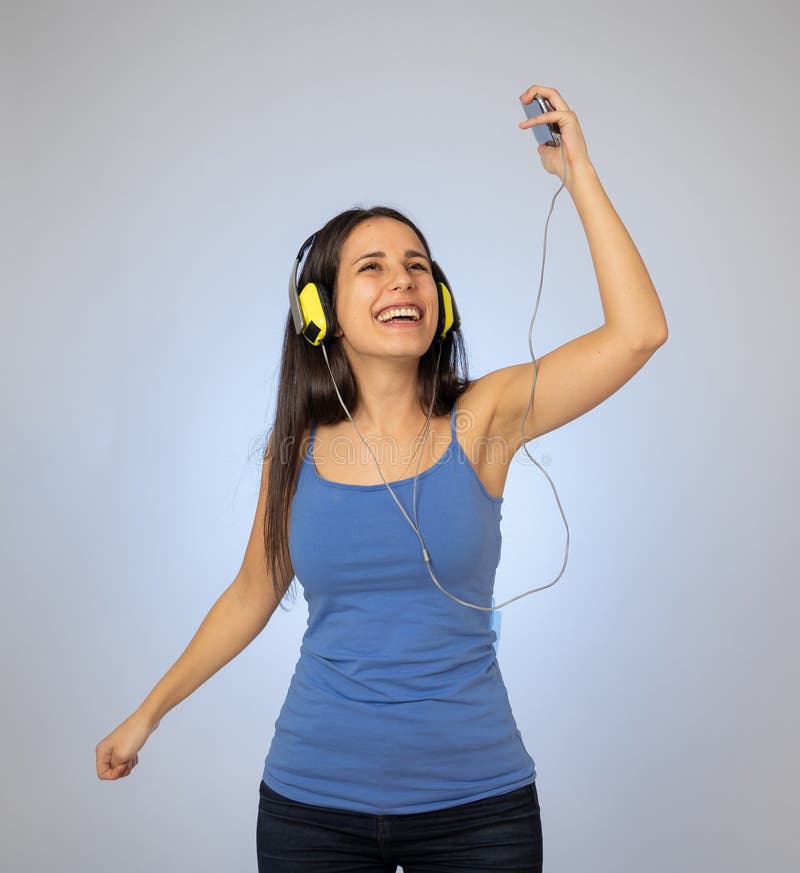 Bella giovane donna in cuffie che ascolta la musica sul telefono cellulare che balla e che canta immagine stock libera da diritti Bella giovane donna in cuffie che ascolta la musica sul telefono cellulare che balla e che canta immagine stock libera da diritti