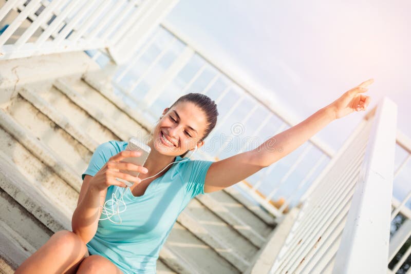 Bella giovane donna felice che si siede sull'i punti e che si rilassa dopo un allenamento duro immagini stock libere da diritti Bella giovane donna felice che si siede sull'i punti e che si rilassa dopo un allenamento duro immagini stock libere da diritti