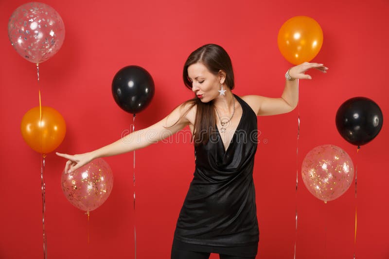 Bella giovane donna in poco vestito nero che celebra le mani di diffusione ballanti che indica dito su fondo rosso luminoso fotografia stock Bella giovane donna in poco vestito nero che celebra le mani di diffusione ballanti che indica dito su fondo rosso luminoso fotografia stock