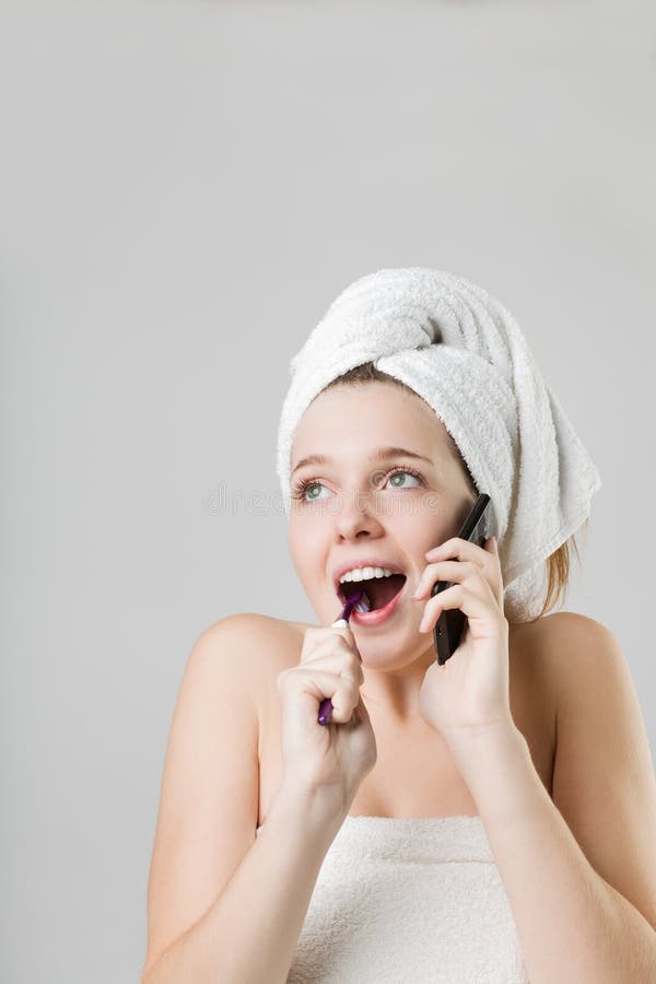 Bella giovane donna sorpresa che parla sul telefono mentre pulendo i suoi denti fotografia stock Bella giovane donna sorpresa che parla sul telefono mentre pulendo i suoi denti fotografia stock