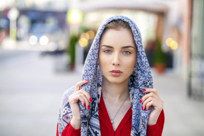 Bella giovane donna in una sciarpa blu sulla città della via di estate immagine stock Bella giovane donna in una sciarpa blu sulla città della via di estate immagine stock