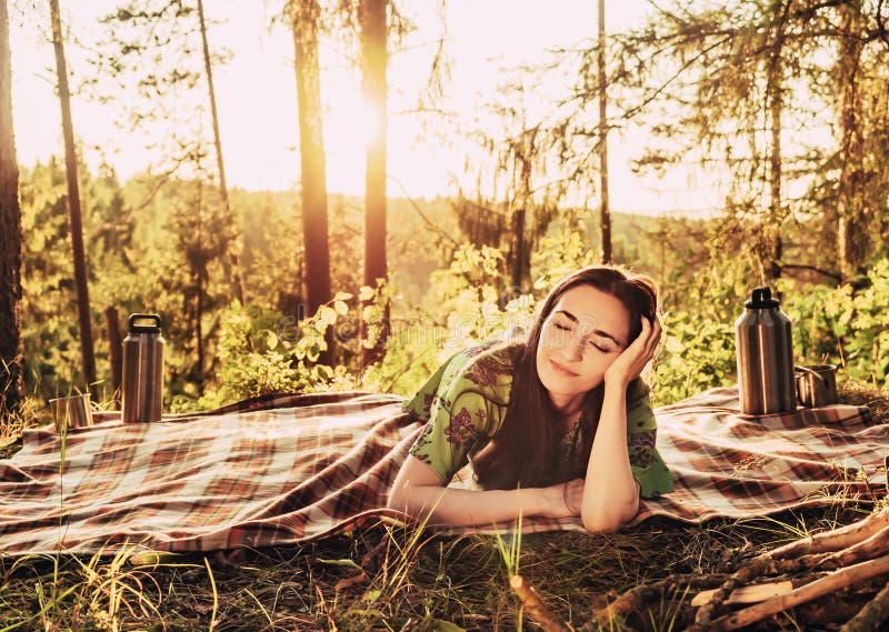Bella giovane ragazza di sogno che si trova su un plaid in una radura della foresta durante la luce solare luminosa di tramonto i immagine stock libera da diritti Bella giovane ragazza di sogno che si trova su un plaid in una radura della foresta durante la luce solare luminosa di tramonto i immagine stock libera da diritti