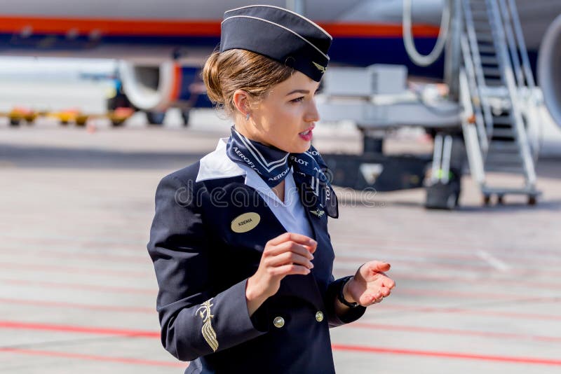 Bella hostess vestita in uniforme blu scuro ufficiale delle linee aeree di Aeroflot sull'aerodromo Aerei di aereo di linea su fon fotografia stock libera da diritti