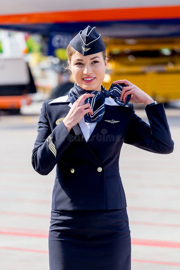 Bella hostess vestita in uniforme blu scuro ufficiale delle linee aeree di Aeroflot sull'aerodromo Aerei di aereo di linea su fon immagine stock