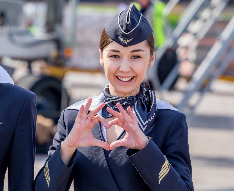 Bella hostess vestita in uniforme blu scuro ufficiale delle linee aeree di Aeroflot sull'aerodromo Aerei di aereo di linea su fon fotografie stock