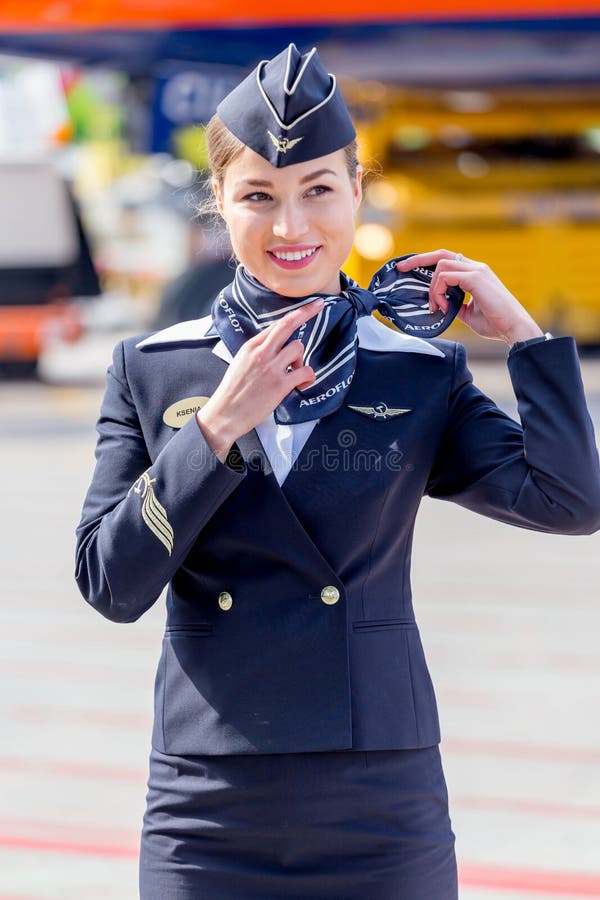 Bella hostess vestita in uniforme blu scuro ufficiale delle linee aeree di Aeroflot sull'aerodromo Aerei di aereo di linea su fon immagine stock
