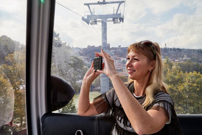 Bella joven atractiva sosteniendo el teléfono celular en las manos y haciendo selfie. viajero en funicular en las montañas imagen de archivo