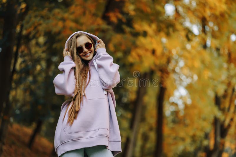 Bella joven sonriente y feliz usando capucha rosa caminando en el parque de otoño. concepto de temporada y personas.