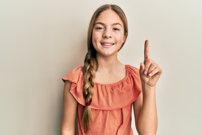 Bella morena pequeña niña con camisa de verano sonriendo con una idea o pregunta apuntando hacia arriba con feliz número de la car imagen de archivo