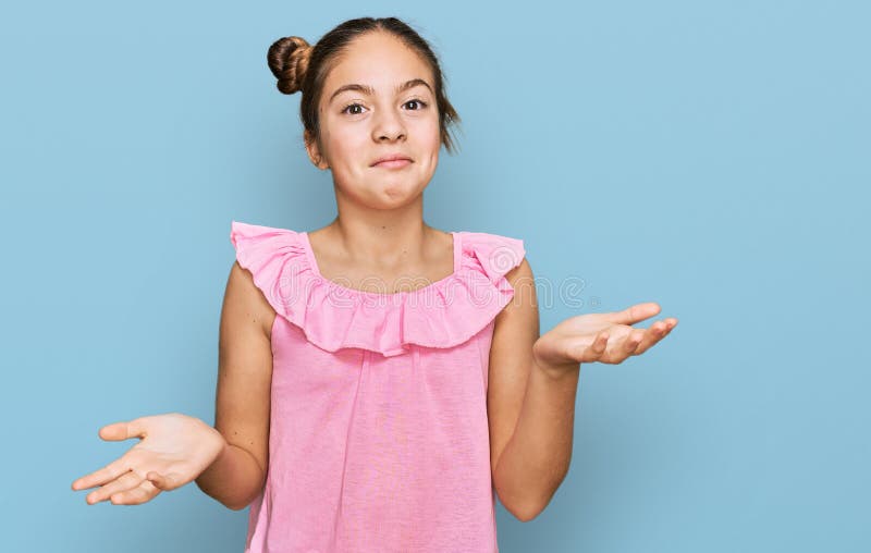 Bella morena pequeña niña con camisa rosa de verano despistada y expresión confusa con brazos y manos levantados fotos de archivo
