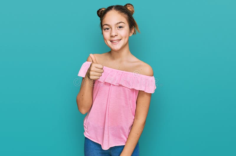 Bella morena pequeña niña con camisa rosa de verano sonriente feliz y pulgar positivo haciendo excelente y señal de aprobación fotos de archivo